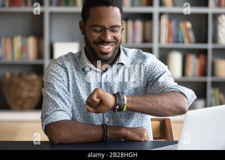 Smiling millennial african american man checking time on wristwatch. Stock Photo