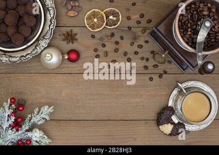 Vintage manual coffee mill, coffee beans, retro metal cup with coffee, silver plate with chocolate truffles and Christmas decorations with snowy pine Stock Photo