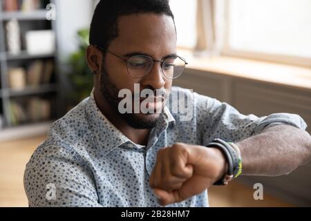 Focused young african ethnic businessman checking time on wristwatch. Stock Photo