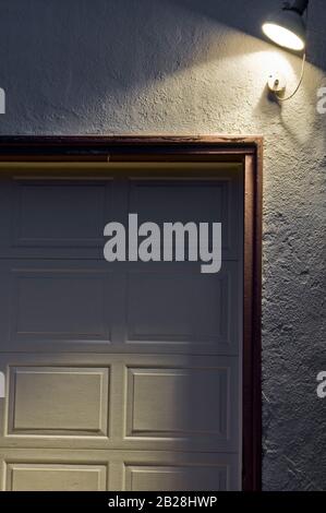 Side light illuminating the old garage door framed with a brown trim on the cream colored stucco wall Stock Photo