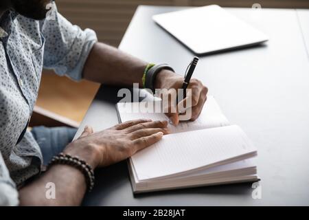 Focused young mixed race businessman writing notes in paper notebook. Stock Photo