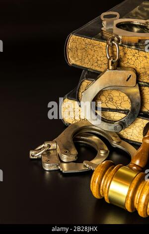 Police handcuffs and books of laws on black background. Wooden gavel and books on wooden table, law concept. Law and order. Stock Photo
