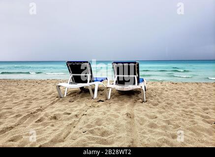 Two loungers, chaise-longues on a cuban beach before storm. Cloudy and windy weather and sky. Stock Photo