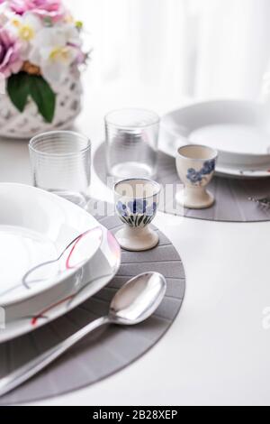 Minimalist white tableware on a white surface dining table in natural light, angled view. Stock Photo
