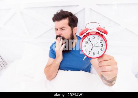 Time to wake up. Healthy habits. Beginning of awesome day. Wake up early every morning. Health benefits of rising early. Waking up early gives more time. Hipster bearded man in bed with alarm clock. Stock Photo