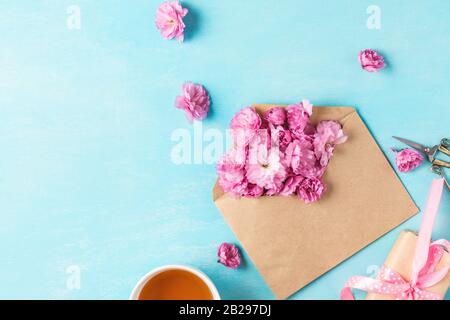 Festive or wedding composition. Spring pink blossom flowers in envelope with cup of tea and gift box on blue background. flat lay. top view with copy Stock Photo