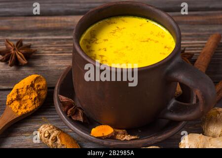 Traditional Indian drink turmeric latte or golden milk with cinnamon, ginger, anise, pepper and turmeric on rustic wooden table. Healthy drink Stock Photo