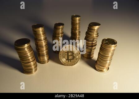Warm light over a pile of coins with Bitcoin symbol placed on a central coin among six pillars of change creating long shadow from right to left Stock Photo