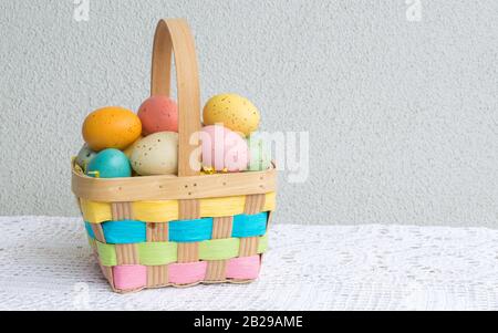 a colorful wicker Easter basket filled with speckled Easter eggs on a white lace table cloth with copy space Stock Photo