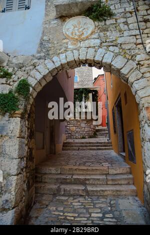 Low angle vertical image of baroque style faded coat of arms above the passage with arch and stairs on the street of Rovinj Croatia Stock Photo