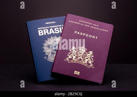 European - Dutch - passport in front of a Brazilian passport on a dark studio surface and background. Concept double nationality. Stock Photo