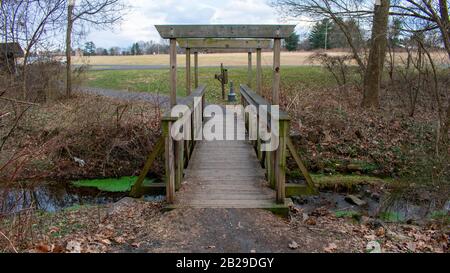 A Wooden Bridge Crossing a Small Stream With Pieces of Wood to Support a Roof Above it Stock Photo