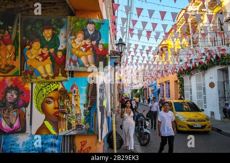 Pedestrians walk by paintings for sale at an artist's studio in the Barrio Getsemaní, Cartagena, Colombia Stock Photo
