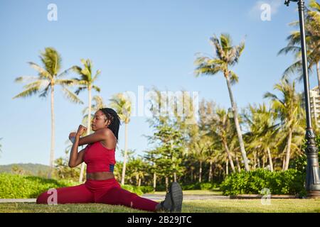 Sportswoman sitting in splits and doing stretching exercise for her arms Stock Photo