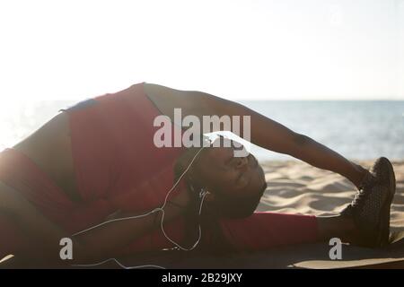 Flexible sportswoman doing splits on sandy beach and bending to her left leg Stock Photo