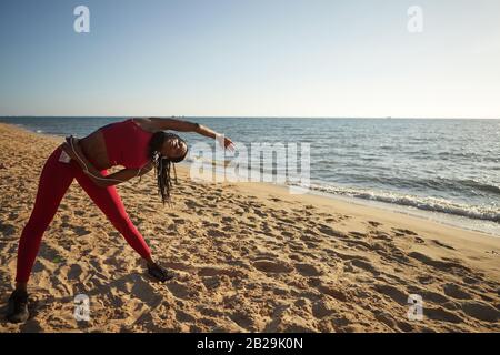 Flexible fit woman standing on sandy beach and bending to her left Stock Photo