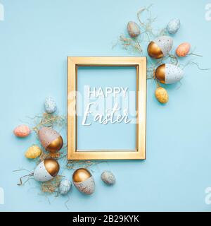 Top view of Easter eggs colored with in different colors arranged around a golden photo frame. Blue background. Happy Easter text. Stock Photo