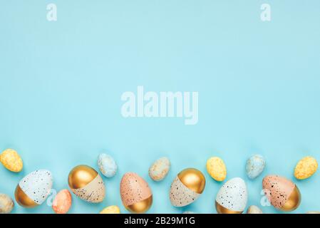 Top view of Easter eggs colored with golden paint and different colors. Blue background. Copy space. Stock Photo