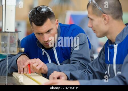 two carpenters are talking while holding papers and ruler Stock Photo