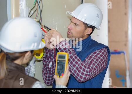 two electricians checking voltage in a wall socket Stock Photo