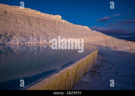Illuminated white Pamukkale travertines with water in foreground. Blue sky in background. Stock Photo