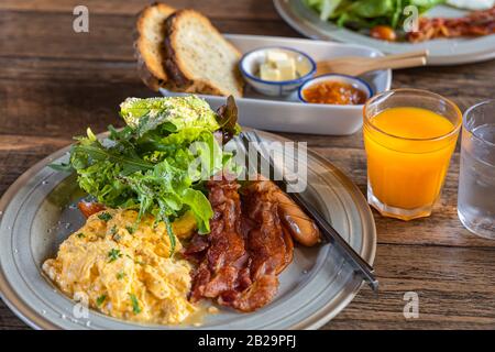 English breakfast-Scrambled eggs, bacon, vegetables, orange juice on wooden table. Stock Photo