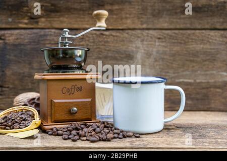 A White tin cup of hot coffee with coffee grinder and coffee bean on the wooden table. Stock Photo