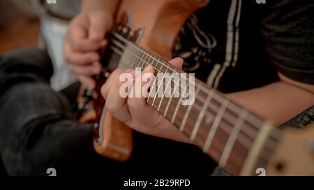 Cropped shot of male musician playing guitar while siting on sofa in music instrument Stock Photo