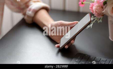 Cropped shot of female holding blank screen smartphone on black table in modern living room Stock Photo