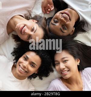 Top view diverse young women friends lying in bed together Stock Photo