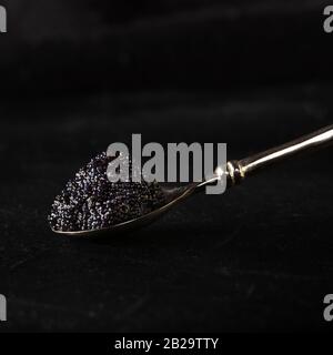 Black caviar on a silver spoon, close-up on a dark background with copy space, square image Stock Photo