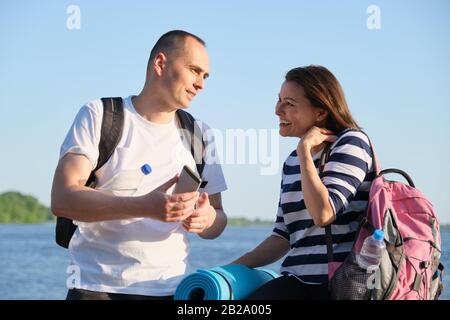 Talking man and woman 40 years old, looking at smartphone Stock Photo