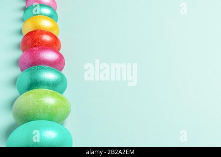 Row of brightly multicolored painted Easter eggs on trendy Neo Mint pastel background. Easter festive layout. Copy space, selective focus. Perspective Stock Photo