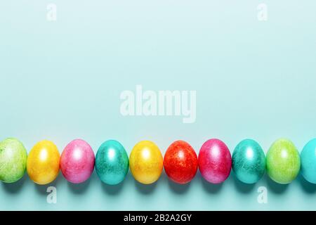 Row of brightly colored Easter eggs with dark shadows on trendy Neo Mint pastel background. Easter festive blank layout. Top view, flat lay, copy spac Stock Photo