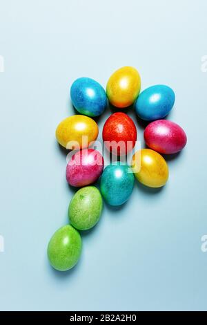 Easter creative festive composition. Colored glossy Easter eggs laid out in form of flower on light blue pastel background. Top view, flat lay. Vertic Stock Photo