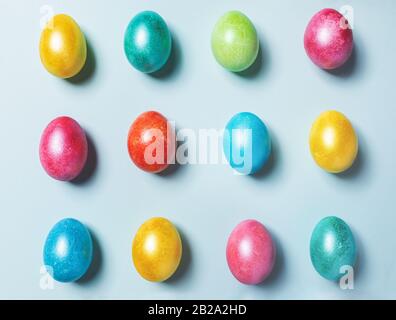 Easter festive knolling composition of brightly multicolored painted glossy Easter eggs laid out on light blue pastel background. Top view, flat lay. Stock Photo