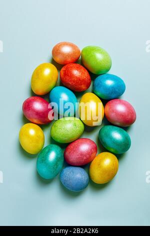 Easter creative festive composition. Lot of colored glossy Easter eggs laid out in form of large Easter egg on light blue pastel background. Top view, Stock Photo