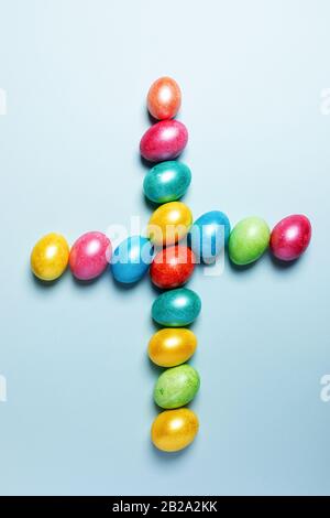 Easter creative festive composition. Colored glossy Easter eggs laid out in shape of cross on light blue pastel background. Top view, flat lay. Vertic Stock Photo