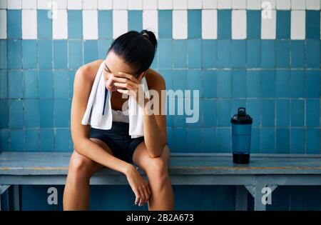 Tired fit woman with a towel in the locker room after hard workout. Stress, sport, failure concept Stock Photo