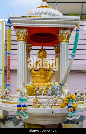 Golden multi-faced buddha statue in a shrine with orange flowers, Bangkok, Thailand Stock Photo