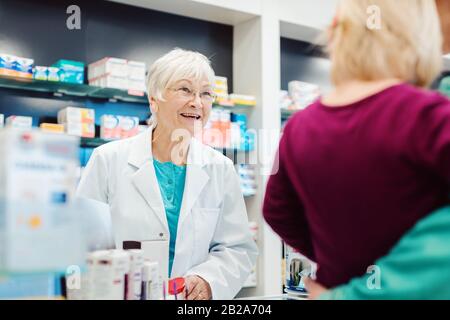 Senior pharmacist talking to mom with her kid Stock Photo