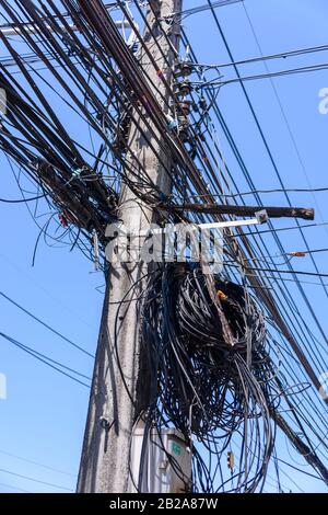 Messy and untidy electrical cables hanging from an electricity pole in Thailand Stock Photo