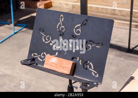 Metal music stand with treble clefs on a street in full sun. Stock Photo