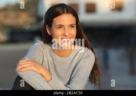 Portrait of a happy teenage girl smiling looking away at sunset in a town Stock Photo