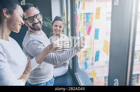 Business people meeting at office and use post notes to share idea. Brainstorming concept. Sticky note on glass wall. Stock Photo