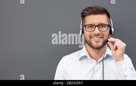 Call center worker isolated on a gray background. Smiling customer support operator at work. Young employee working with a headset. Stock Photo