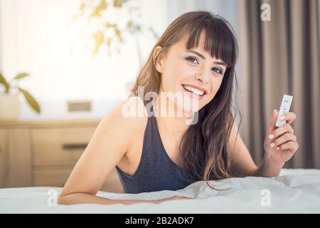Young beautiful woman holding a pregnancy test. Enjoys a positive result. He is happy because he will be a mom. Stock Photo