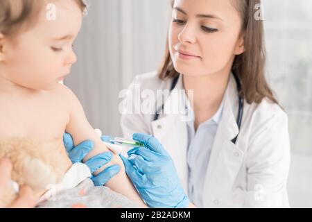 Young woman pediatrician performs a vaccination of a little girl. The girl is holding a mascot. Stock Photo