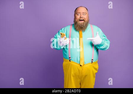 Crazy shocked bearded man big abdomen use smartphone browse social media promo point index finger device wear turquoise pink suspenders yellow Stock Photo