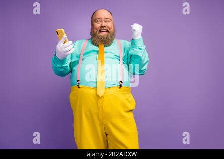 Low angle view photo ecstatic bearded man big belly use smartphone achieve win loterry raise fists scream wear white gloves teal pink suspenders Stock Photo